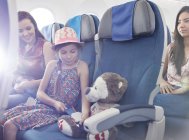 Girl fastening seat belt on stuffed animal on airplane — Stock Photo