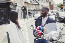 Lächelnder junger Geschäftsmann auf Motorroller im Gespräch mit Freund auf der Straße — Stockfoto