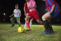 Jóvenes jugadoras de fútbol jugando en el campo por la noche, corriendo por la pelota - foto de stock