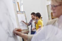 Artists discussing sketch at easel in art class studio — Stock Photo