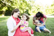 Lesbianas madres jugando, cosquillas niños en verano patio de hierba - foto de stock