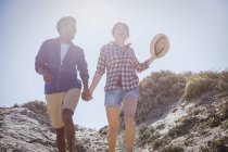 Multi-ethnisches Paar zu Fuß, Händchen haltend auf sonnigem Sommerstrandweg — Stockfoto