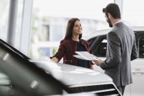 Car saleswoman showing brochure to male customer in car dealership showroom — Stock Photo