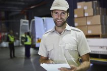 Portrait smiling truck driver worker with clipboard at distribution warehouse loading dock — Stock Photo