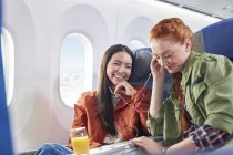 Young women friends sharing headphones, listening to music on airplane — Stock Photo