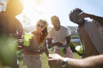 Смеющиеся юные друзья пьют и зависают в солнечном летнем парке — стоковое фото