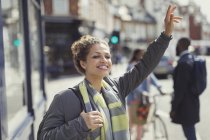 Lächelnde junge Frau bejubelt Taxi auf sonniger Stadtstraße — Stockfoto