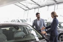 Car saleswoman showing new car to male customer in car dealership showroom — Stock Photo