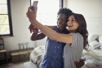 Sorridente coppia lesbica abbracciare, prendendo selfie con fotocamera telefono in camera da letto — Foto stock
