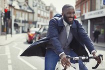 Giovane uomo d'affari sorridente pendolarismo, in bicicletta sulla strada urbana soleggiata — Foto stock