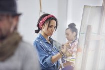 Focused female artist painting at easel in art class studio — Stock Photo