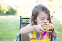 Preschool girl eating messy cheeseburger on patio — Stock Photo