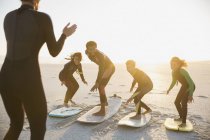 Instrutor de surfistas ensinando família em pranchas de surf surfando na ensolarada praia de verão ao pôr do sol — Fotografia de Stock