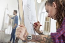 Зосереджена художниця з татуюванням на мольберті в студії арт-класу — стокове фото