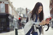 Young woman commuting on bicycle, texting with cell phone on sunny urban street — Stock Photo
