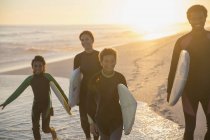 Сімейні серфери, що йдуть з дошками для серфінгу на сонячному літньому заході сонця океанський пляж — стокове фото