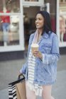 Smiling woman walking along storefront with coffee and shopping bags — Stock Photo