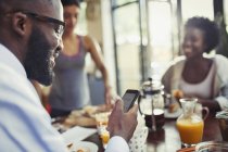 Giovane uomo sms con smart phone al tavolo della cucina — Foto stock