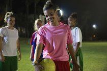 Ritratto sorridente, giovane calciatrice sicura di sé con palla sul campo di notte — Foto stock