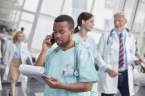 Чоловіча медсестра з буфетом розмовляє на мобільному телефоні в лікарняному коридорі — стокове фото