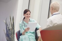 Усміхнена медсестра з буфером розмовляє з лікарем в лікарні — стокове фото