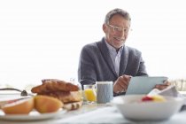 Senior nutzt digitales Tablet beim Frühstück auf der Terrasse — Stockfoto