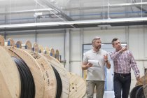 Supervisore maschile e lavoratore con appunti che camminano lungo bobine in fabbrica di fibre ottiche — Foto stock