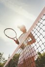 Jogadora de tênis focada com raquete de tênis em pé na rede na quadra de tênis ensolarada — Fotografia de Stock
