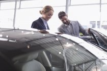 Autoverkäufer zeigt Kundin im Autohaus Neuwagen — Stockfoto