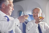 Empresário brindando copos de uísque em primeira classe no avião — Fotografia de Stock