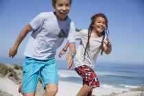 Играющие брат и сестра бегают по солнечному летнему пляжу — стоковое фото