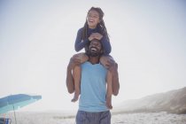 Грайливий батько носить дочку на плечах на сонячному літньому пляжі — стокове фото