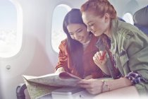 Young women friends looking at map on airplane — Stock Photo