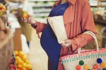 Mujer embarazada comprando manzanas en la tienda de comestibles - foto de stock
