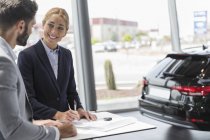 Продавец автомобилей и мужчина подписывают контрактные документы в автосалоне — стоковое фото