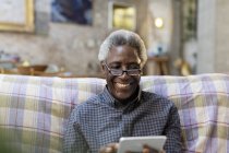 Uomo anziano sorridente utilizzando tablet digitale sul divano — Foto stock