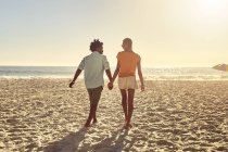Young couple holding hands, walking on sunny summer beach — Stock Photo