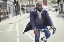 Junge männliche Geschäftsmann pendelt mit dem Fahrrad auf sonniger Stadtstraße — Stockfoto
