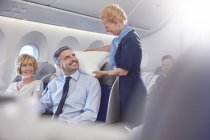 Lächelnde Flugbegleiterin richtet Kopfkissen für Geschäftsmann in der ersten Klasse im Flugzeug ein — Stockfoto