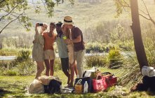 Молоді друзі беруть селфі з телефоном на сонячному літньому березі річки — стокове фото