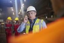 Supervisor de trabajadores siderúrgicos hablando por teléfono inteligente en fábrica de acero - foto de stock