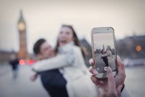 Personal perspective, playful couple hugging and being photographed with camera phone near Big Ben, London, UK — Stock Photo