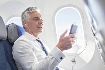 Businessman listening to music with headphones and mp3 player on airplane — Stock Photo