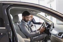 Car saleswoman and male customer in driver?s seat of new car in car dealership showroom — Stock Photo