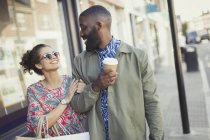 Smiling young couple with coffee walking arm in arm along storefronts — Stock Photo
