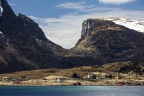 Montañas sobre remotas casas costeras, Krystad, Lofoten, Noruega - foto de stock