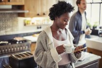 Женщина пьет кофе, пишет смс со смартфона на кухне — стоковое фото