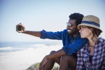 Casal multi-étnico tomando selfie na praia ensolarada de verão — Fotografia de Stock