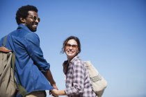 Портрет улыбающейся, нежной многонациональной пары, держащейся за руки под солнечным летним голубым небом — стоковое фото