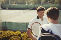 Giovani tennisti maschi che parlano sopra campi da tennis soleggiati — Foto stock